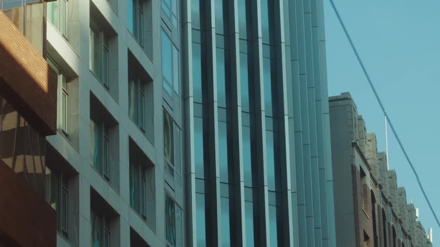 A static shot of modern city buildings with glass and stone exteriors against a clear blue sky