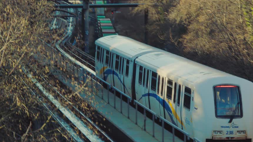 A high-angle shot captures a white commuter train crossing an elevated track and heading towards a distant city skyline