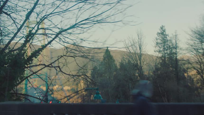 Driving through a forest landscape, the view opens up to reveal the Lions Gate Bridge in Vancouver with mountains in the background