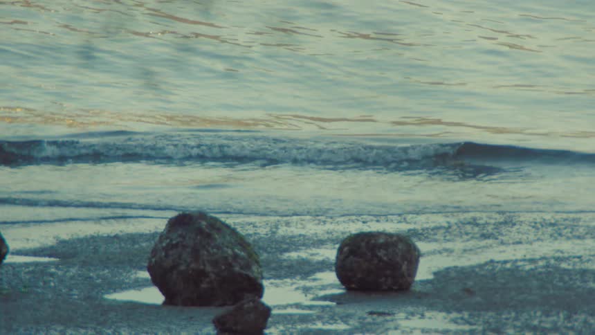 Slow motion capture of tranquil waves lapping onto a sandy and rocky shore during a peaceful golden hour