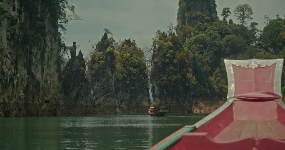 View from a traditional red long-tail boat of majestic limestone karsts and lush jungle surrounding a serene tropical lake