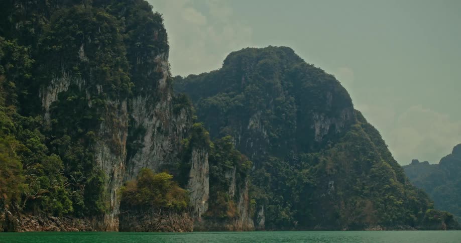 Towering jungle-covered limestone mountains rise from the serene, emerald waters of a tropical lake
