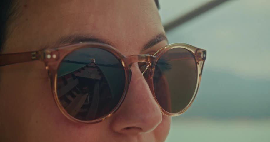 The reflection of a traditional Thai long-tail boat is captured in the sunglasses of a woman enjoying a boat trip