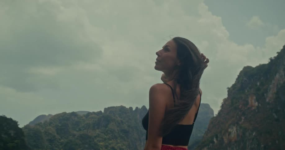 A serene woman with long hair blowing in the wind looks out at the breathtaking mountain scenery in slow motion