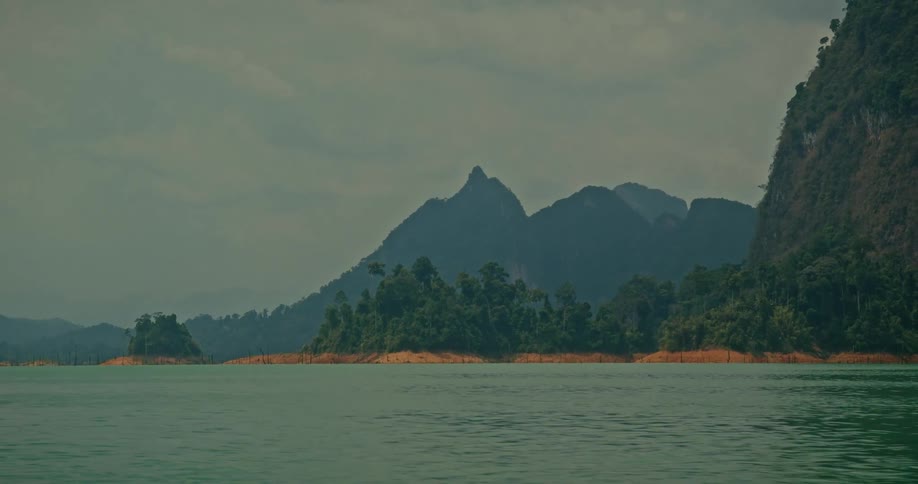 Tilting up from the tranquil green water to reveal a stunning tropical mountain landscape