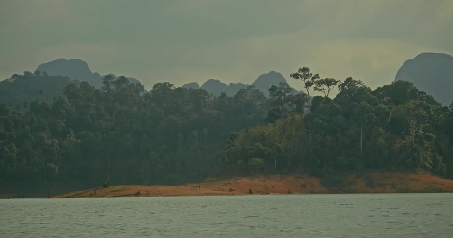 A serene view of a vast lake with a lush, forested shoreline and hazy mountains in the distance