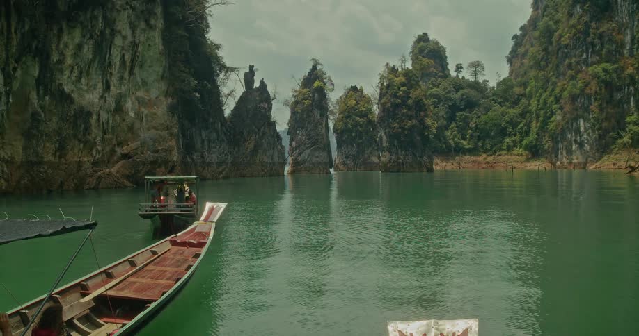 Traditional long-tail boats float on a tranquil lake surrounded by majestic limestone cliffs in Khao Sok National Park, Thailand