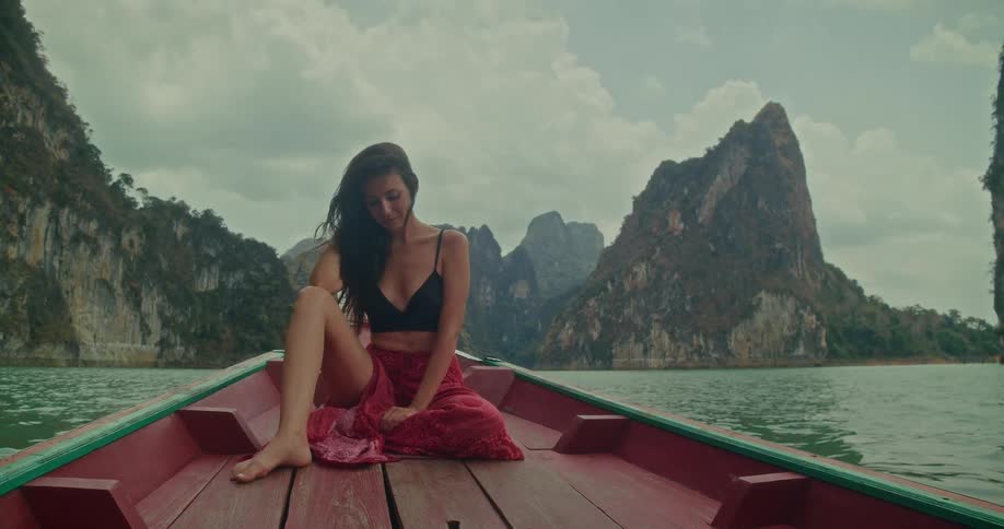 A beautiful woman with long hair enjoys a serene journey on a traditional boat across a stunning lake surrounded by majestic cliffs