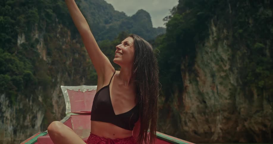 A smiling young woman on a boat journey through a spectacular jungle river canyon raises her arm in a gesture of freedom and joy