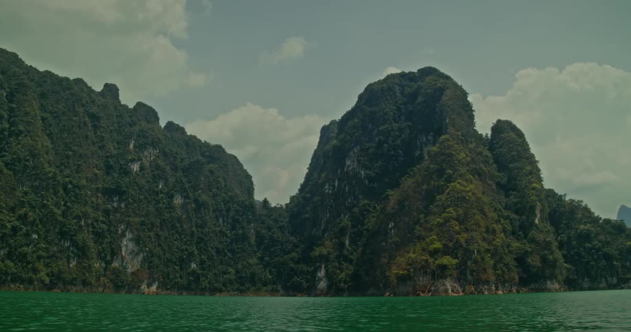 A majestic view from a boat on a tranquil green lake, surrounded by towering limestone mountains covered in lush jungle