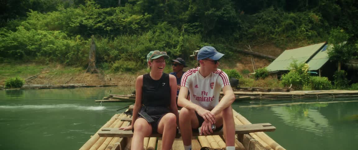 A happy young couple enjoys a peaceful bamboo raft ride down a serene river surrounded by lush tropical jungle