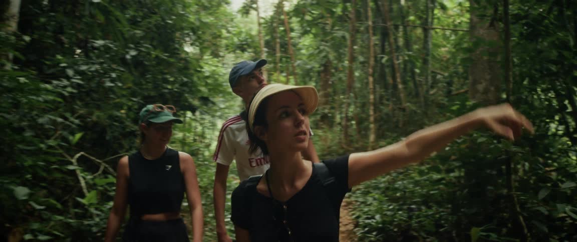 A curious woman points out a discovery to her friends while they hike along a path in a dense tropical jungle