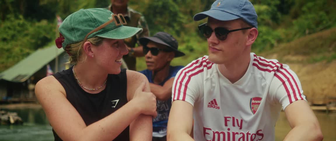 A young couple in casual attire share a happy conversation during a boat trip through a tropical jungle