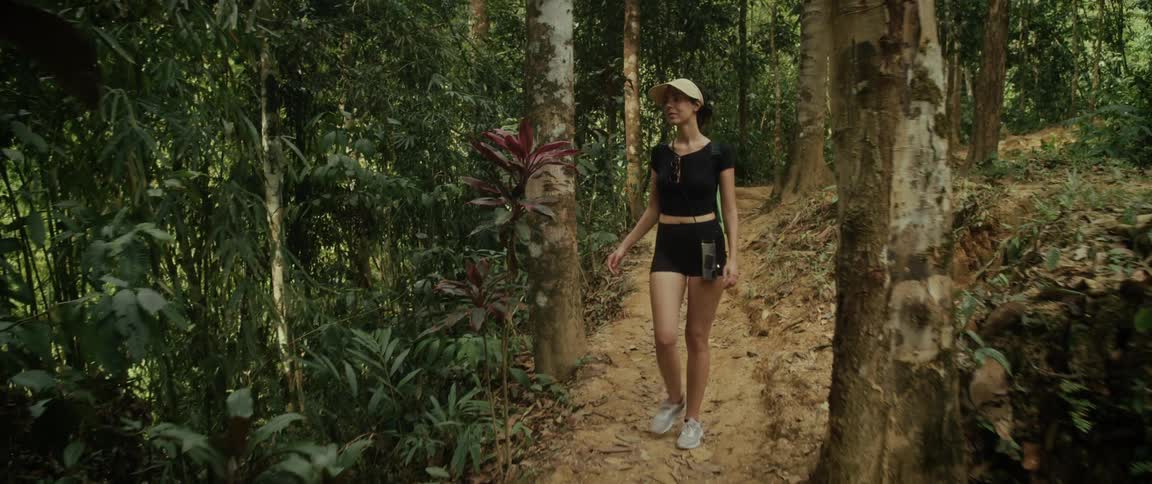 A young woman in activewear enjoys a scenic hike on a dirt trail through a lush tropical jungle