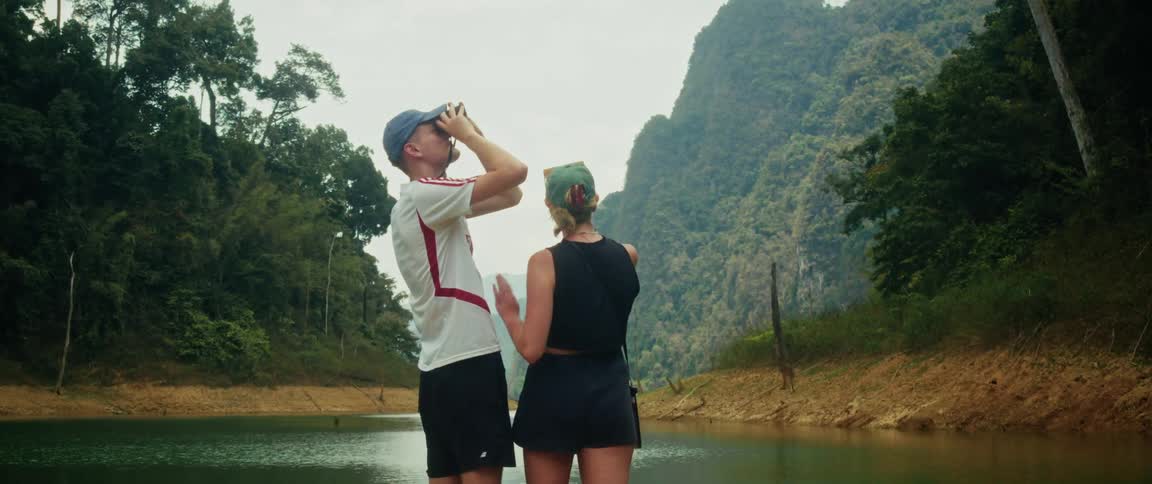 A young couple enjoys a serene boat trip, using binoculars to watch for wildlife and admire the vast tropical mountains surrounding the lake