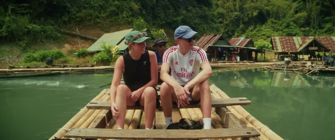 A young couple enjoys a peaceful ride on a bamboo raft down a scenic river through a lush tropical jungle