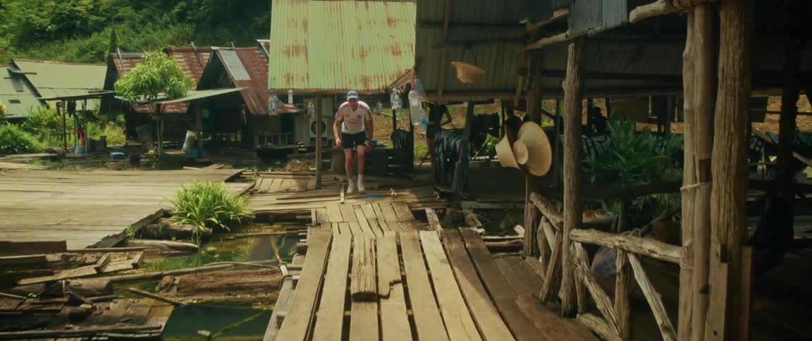 A male traveler explores a rustic floating village, walking carefully across old wooden platforms on a sunny day in Thailand