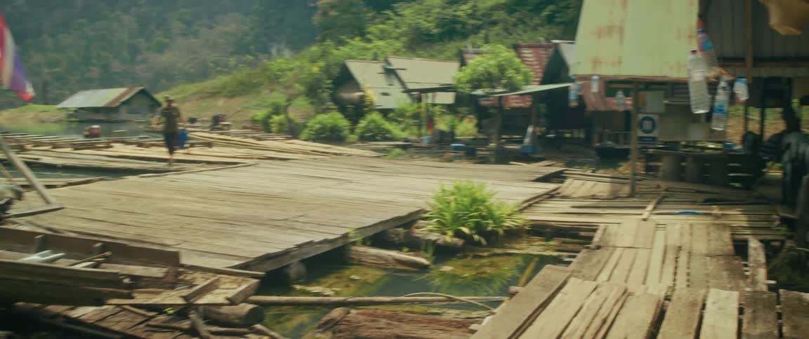 A man carries supplies across the wooden walkways of a rustic floating village on a lake in Thailand
