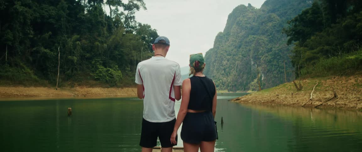 Rear view of a young couple exploring a serene tropical lake on a traditional bamboo raft