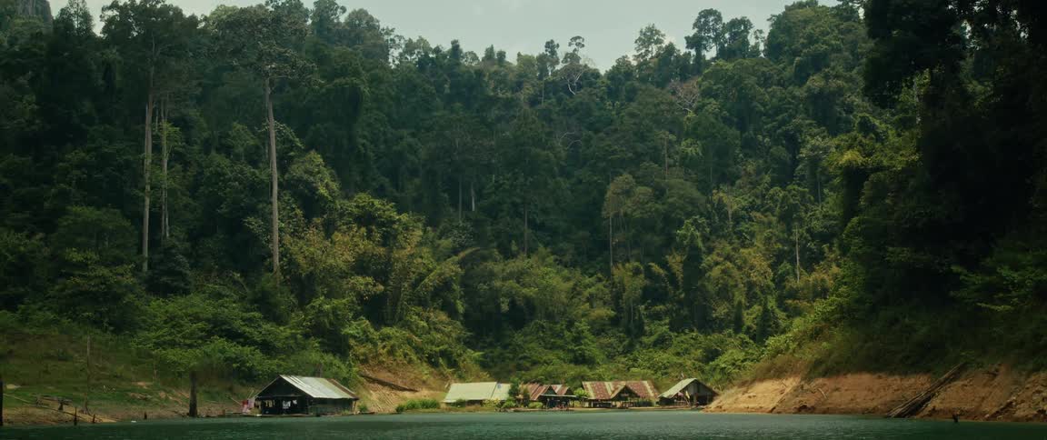 A serene, wide shot of a rustic floating village on a calm lake nestled at the foot of a dense tropical rainforest