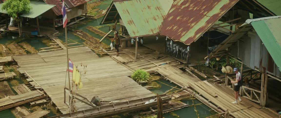 Tourists and locals walk across rickety wooden walkways in a traditional floating village on a river in the Thai jungle