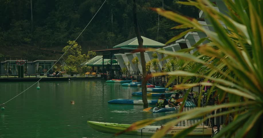 A tranquil view of a lakeside resort reveals colorful kayaks docked by floating bungalows nestled in a lush green forest