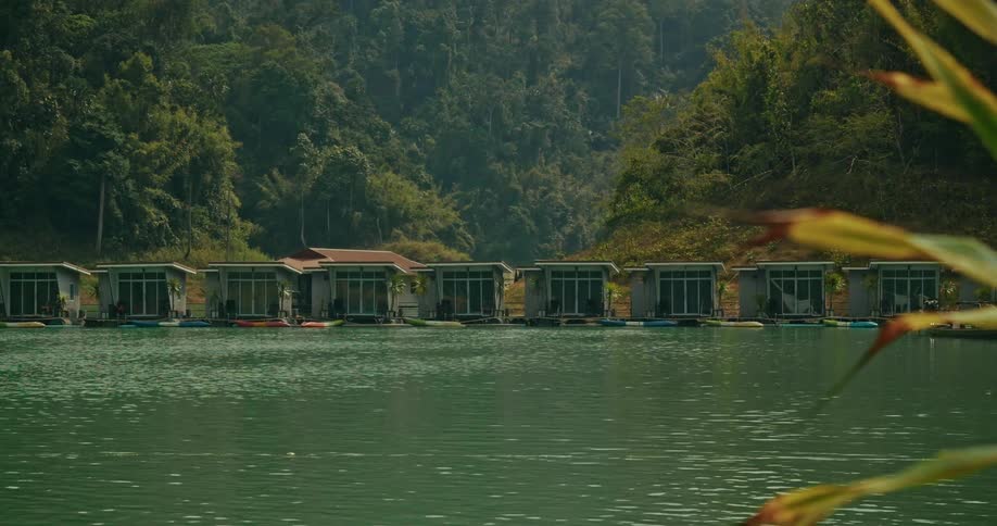 A row of modern floating bungalow resort cabins on a serene lake surrounded by a lush green tropical forest