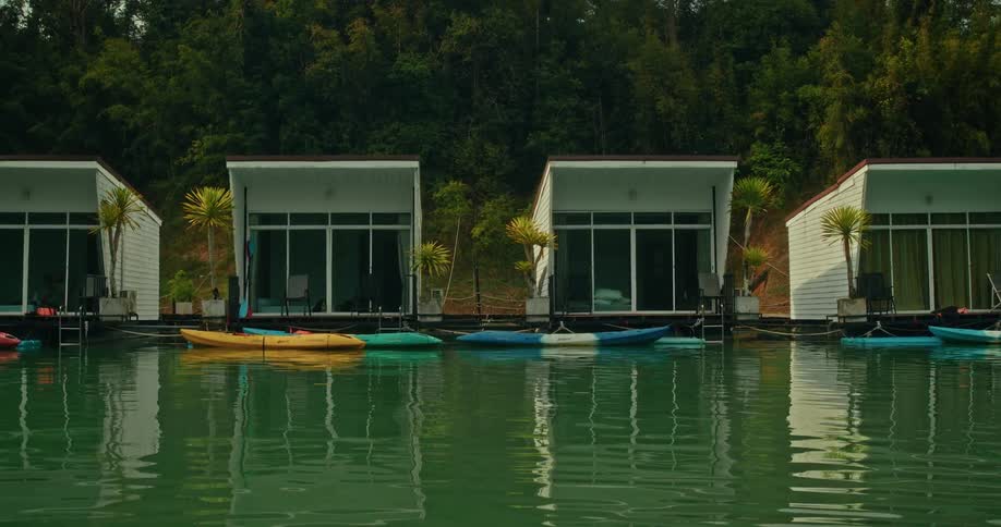 A serene view of modern floating resort bungalows with kayaks on calm green water, nestled against a verdant forest