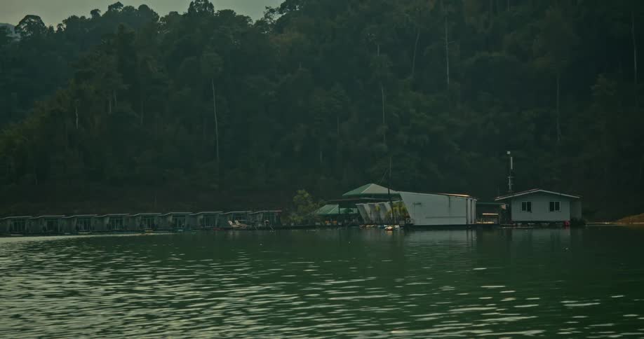 A time-lapse of a secluded floating resort on a calm lake as the sun sets behind a dense tropical forest
