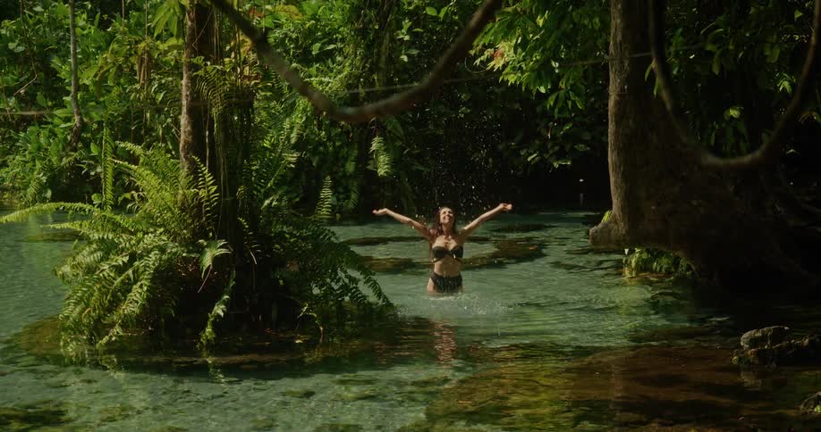 A carefree woman in a bikini splashes joyfully in a pristine jungle river, surrounded by lush tropical foliage