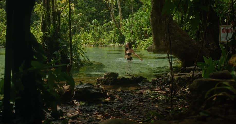 A beautiful woman in a bikini is revealed enjoying and splashing water in a pristine, secluded jungle river
