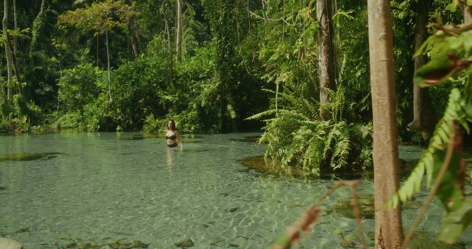 Tracking shot reveals a beautiful woman bathing in a natural spring surrounded by a lush tropical rainforest