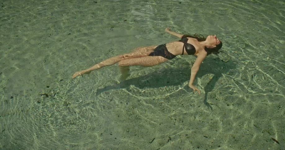 A woman in a bikini peacefully floats on her back in a crystal-clear natural spring surrounded by a lush tropical jungle