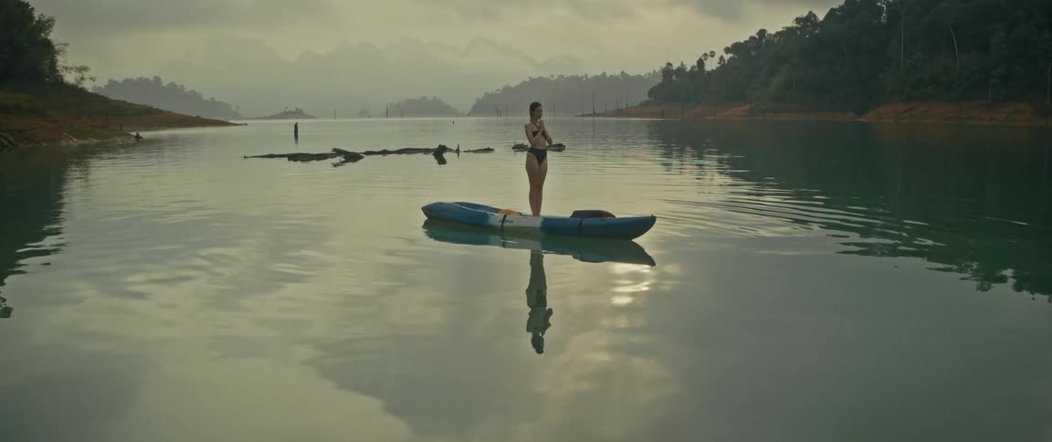 A woman finds her balance while doing yoga on a kayak, surrounded by the tranquil beauty of a misty mountain lake