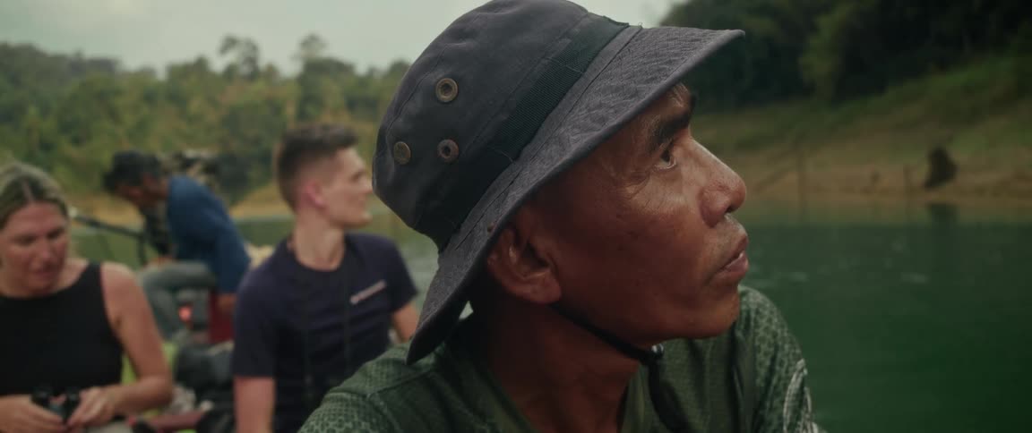 A local guide in a bucket hat looks on intently while leading a tour on a river through the lush jungle
