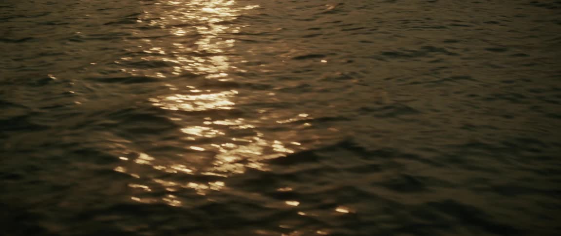 A serene close-up of golden sunlight glinting off the dark, gentle waves of the ocean at sunset