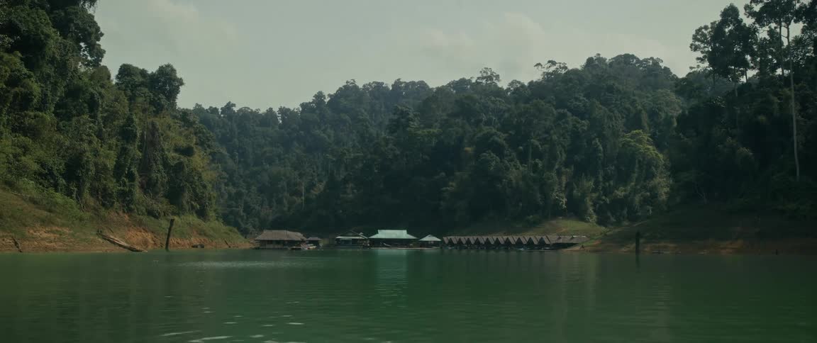 A serene view of a floating bungalow resort nestled on a tranquil lake surrounded by a lush tropical rainforest