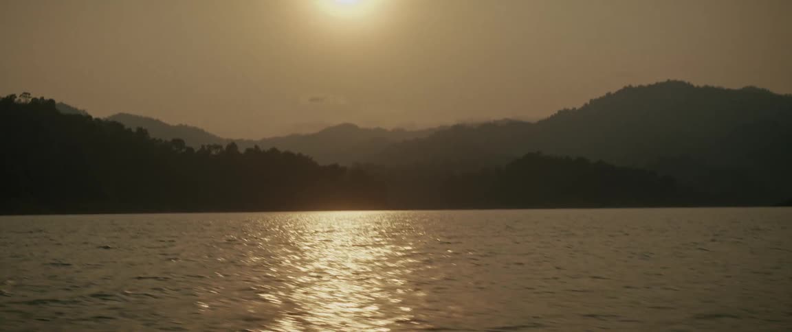 A golden sunset reflects on a serene lake, revealing a beautiful mountainous landscape in the background