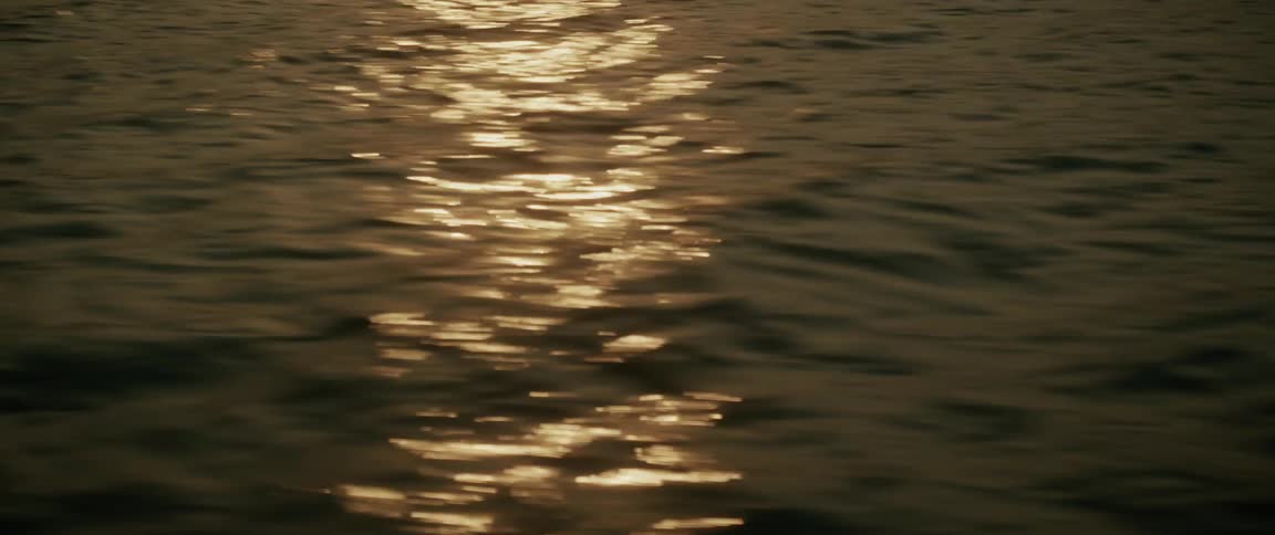The golden sun sets over a tranquil lake, its shimmering reflection rippling across the water's surface