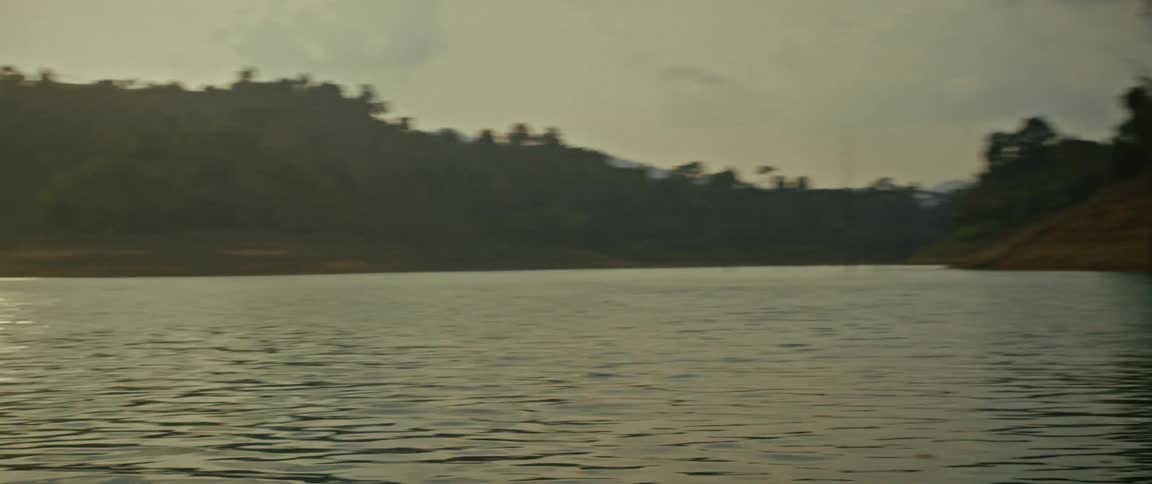 A young woman sits on the bow of a traditional longtail boat, using binoculars to watch wild boars on the shore of a jungle lake