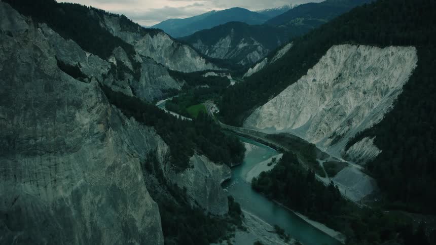 An epic aerial view captures the moody landscape of the Rhine Gorge in Switzerland, where a turquoise river carves its path through forested mountains