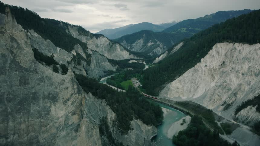 A stunning aerial view shows a red train journeying through the majestic and moody Rhine Gorge, also known as the Swiss Grand Canyon
