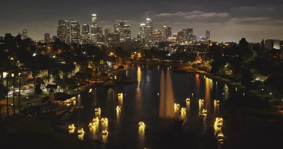 A beautiful night view of the Downtown Los Angeles skyline over Echo Park Lake, featuring a water fountain and glowing swan paddle boats