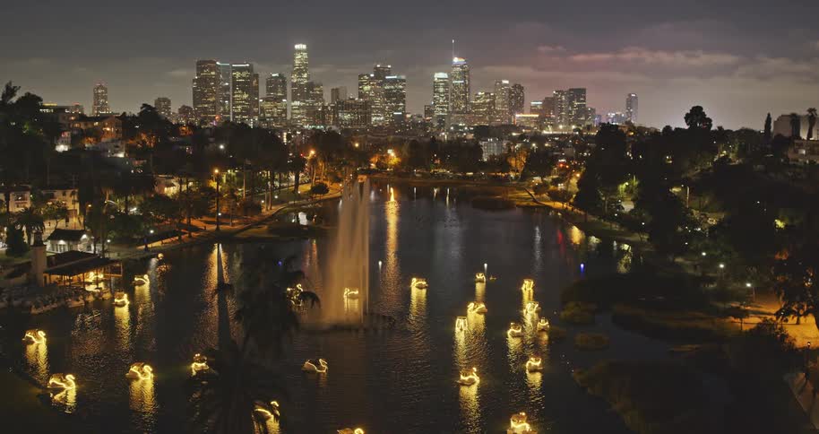 A beautiful aerial view of the downtown Los Angeles skyline at night, moving over Echo Park Lake with its glowing swan boats and a magnificent fountain
