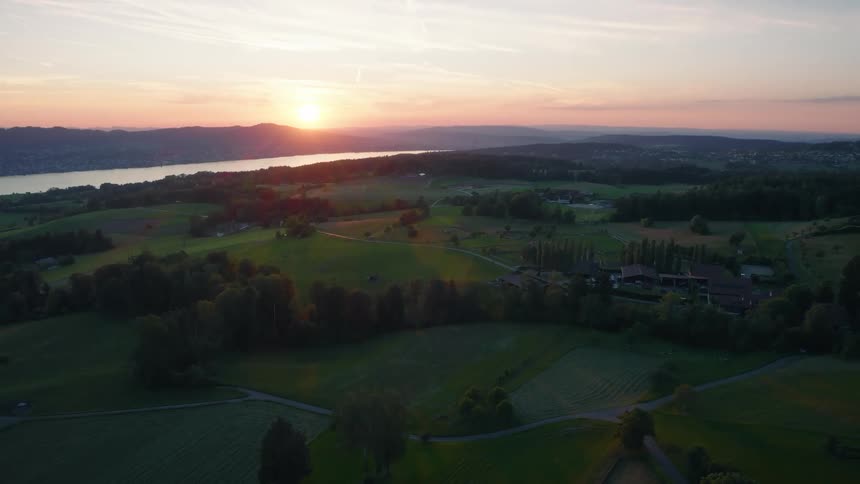 A breathtaking aerial view captures the Swiss countryside and Lake Zurich basking in the warm glow of a beautiful sunset