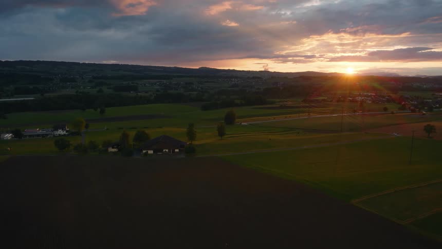 A stunning static aerial shot captures the golden sunset over a vast rural landscape with green and brown fields