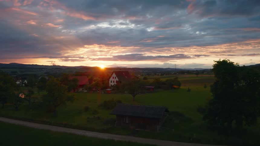 An aerial view of a picturesque farmstead nestled in the green countryside during a beautiful, dramatic sunset