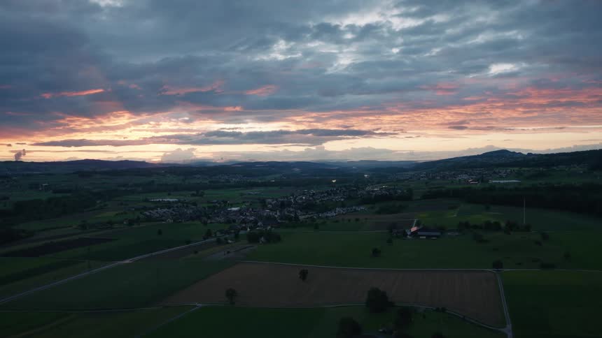 A stunning wide aerial view of a picturesque valley with farmlands and a small town under a beautiful, cloudy sunset