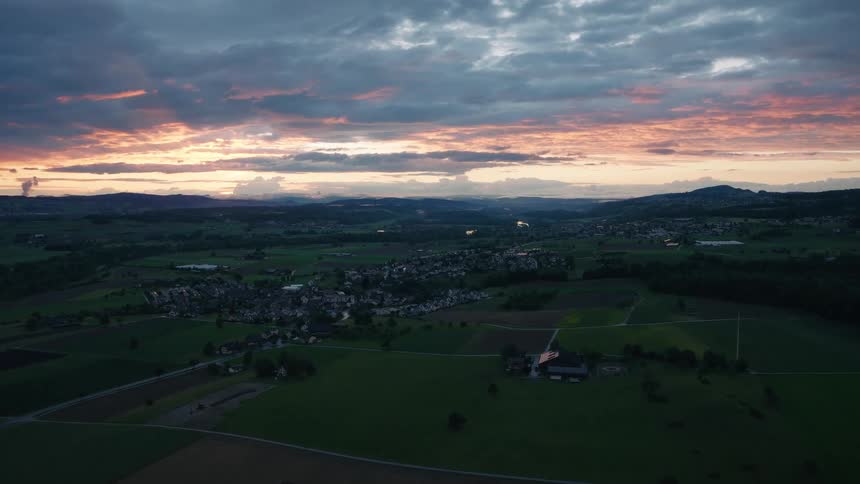 Tranquil aerial view of a picturesque countryside village nestled among green fields under a vibrant sunset sky