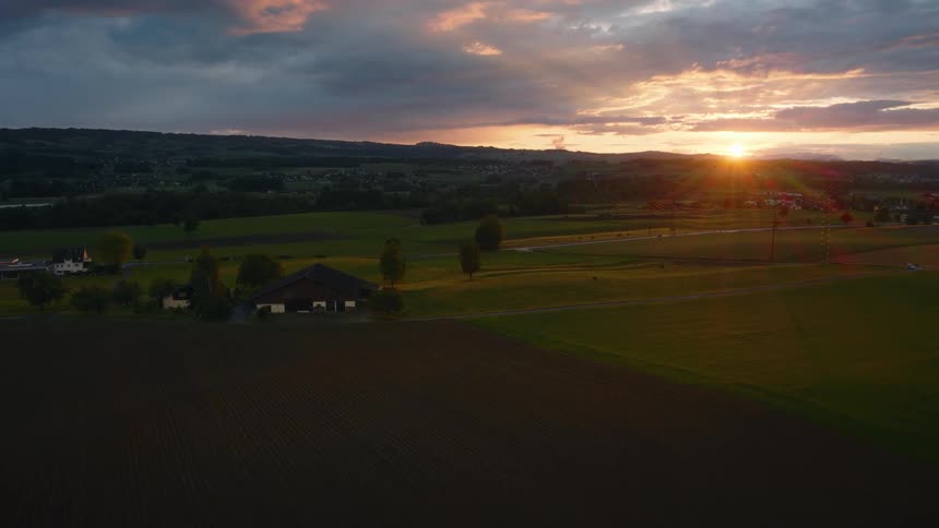 A stunning aerial view of a rural landscape with a farmhouse and fields bathed in the golden light of a dramatic sunset